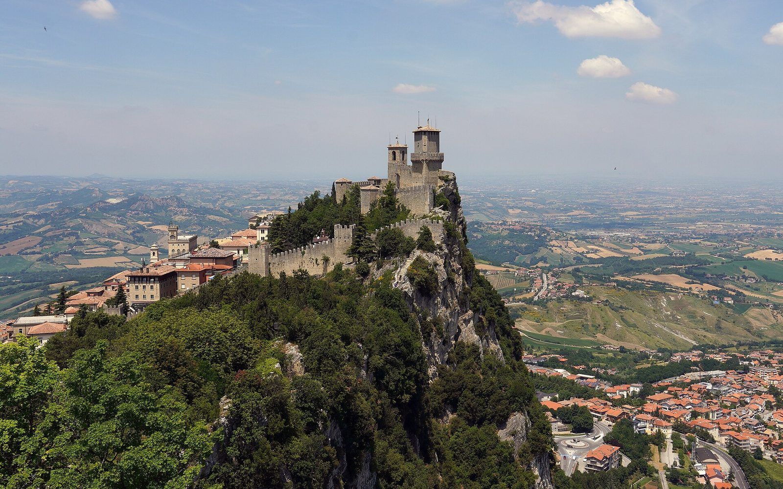 A sweeping view from a San Marino terrace over the Emilia-Romagna countryside towards the distant Adriatic coast at golden hour
