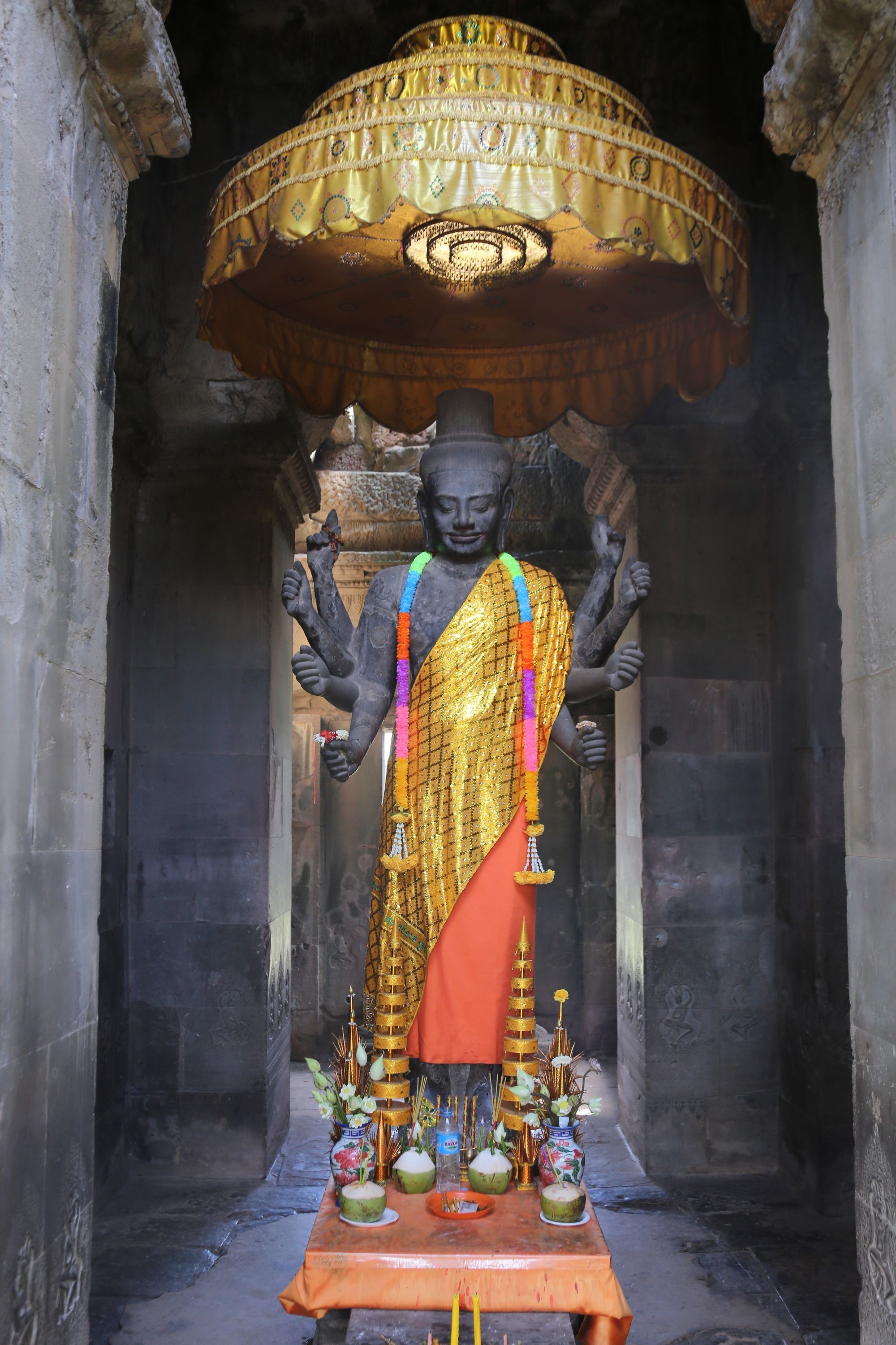 The eight-armed Ta Reach Vishnu statue draped in saffron cloth at Angkor Wat's west entrance, with offerings at its base