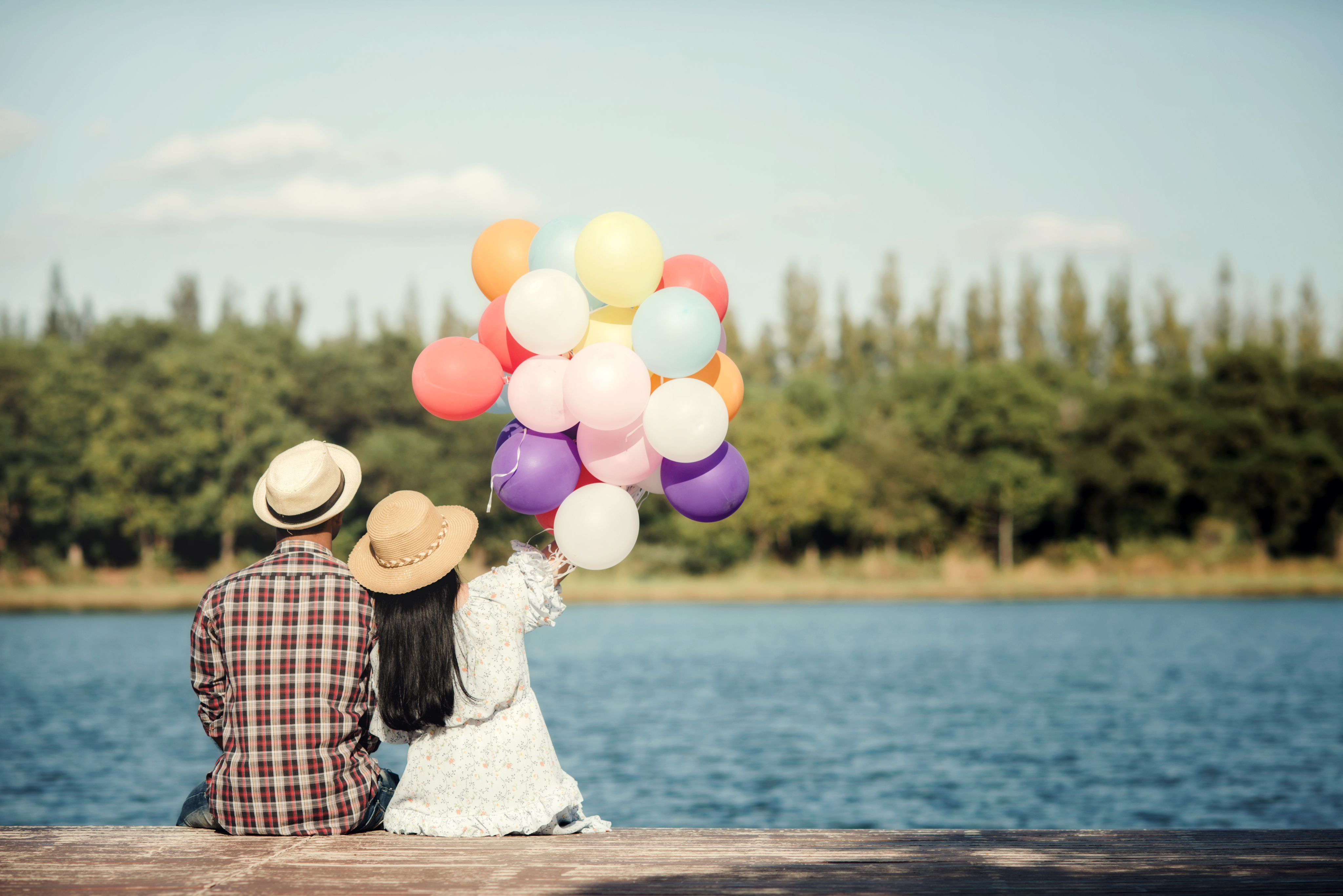 A couple by a lake holding colourful balloons